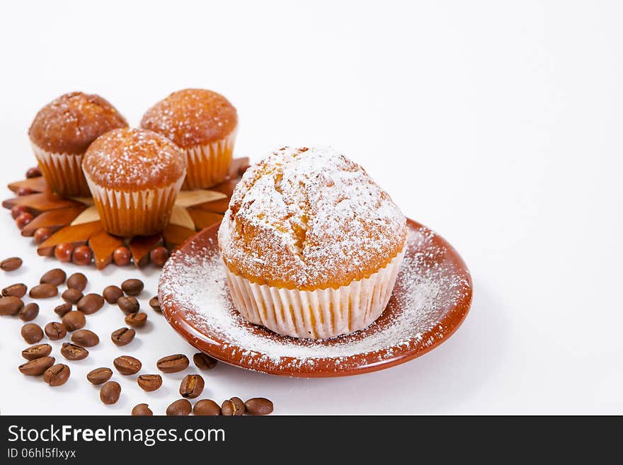 Fresh muffins with powdered sugar and coffee beans on a white background