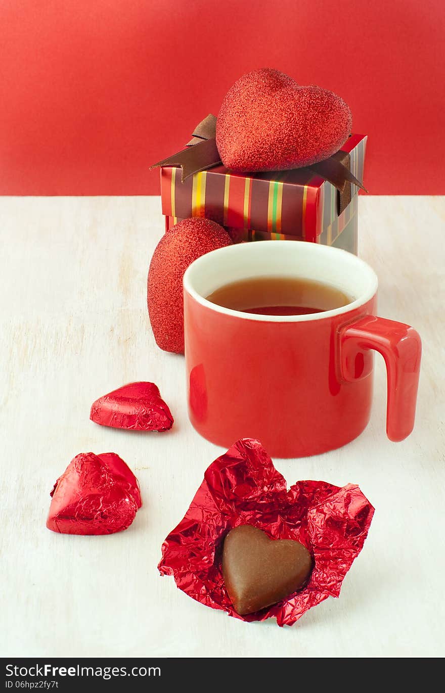 Heart shaped chocolates a cup of tea in a red cup and a gift box. Heart shaped chocolates a cup of tea in a red cup and a gift box