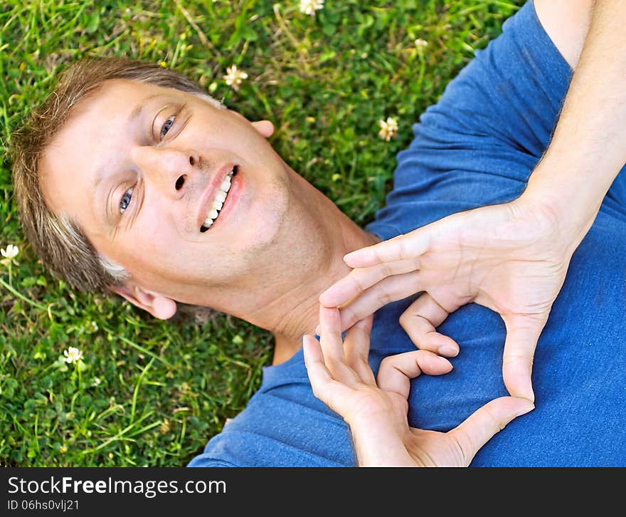 Man lying on grass showing a heart with his hands. Man lying on grass showing a heart with his hands