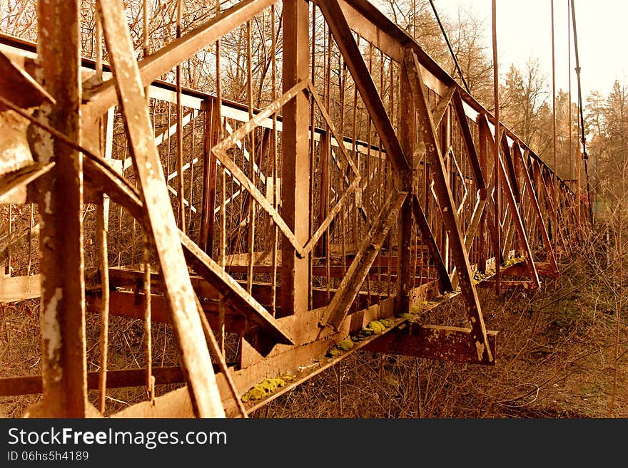 The photo shows an outdated rusty bridge in the forest.