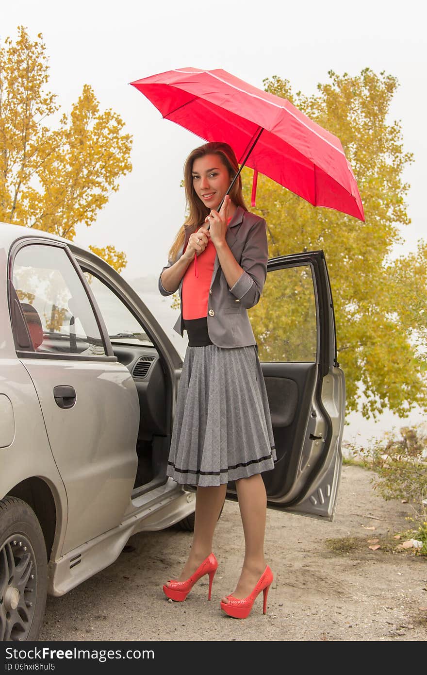 Happy woman outdoor in autamn with red umbrella near the car. Happy woman outdoor in autamn with red umbrella near the car