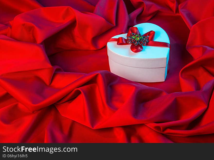 Love card. white heart with a red ribbon on a red fabric in blue lighting from right. Love card. white heart with a red ribbon on a red fabric in blue lighting from right