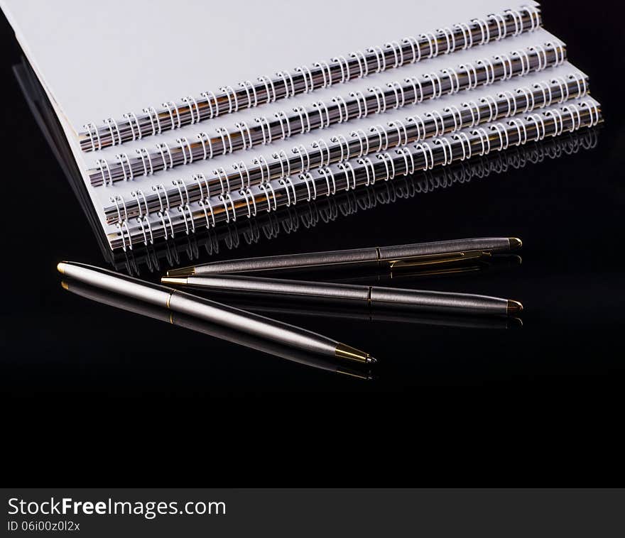 Image of three notebooks and three pens on a black background