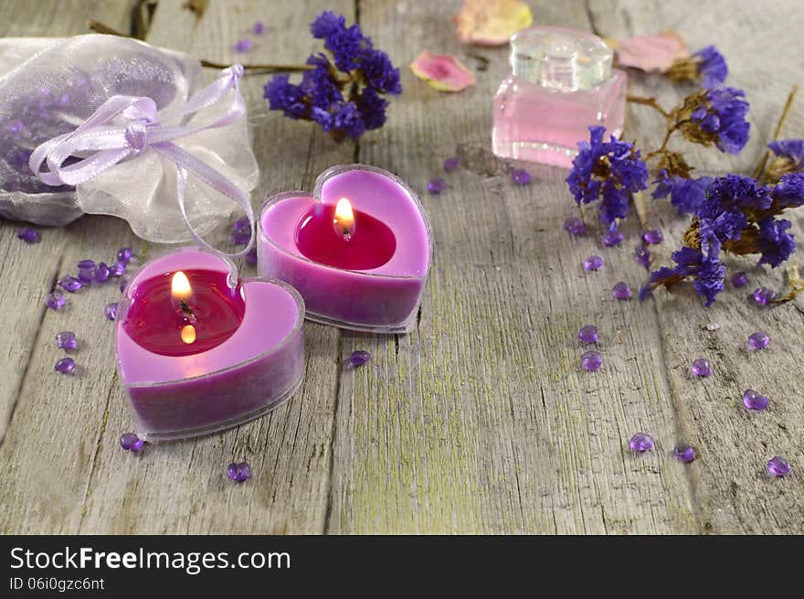 Lilac candles with blue flowers and perfume on wood background