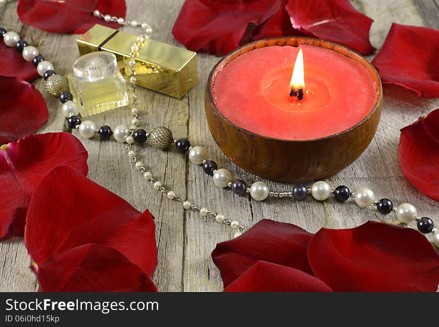 Big red candle with jewelry and rose petals on wood