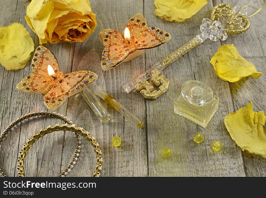 Still life with yellow perfume, the golden key, butterfly candles and jewelry on wood. Still life with yellow perfume, the golden key, butterfly candles and jewelry on wood