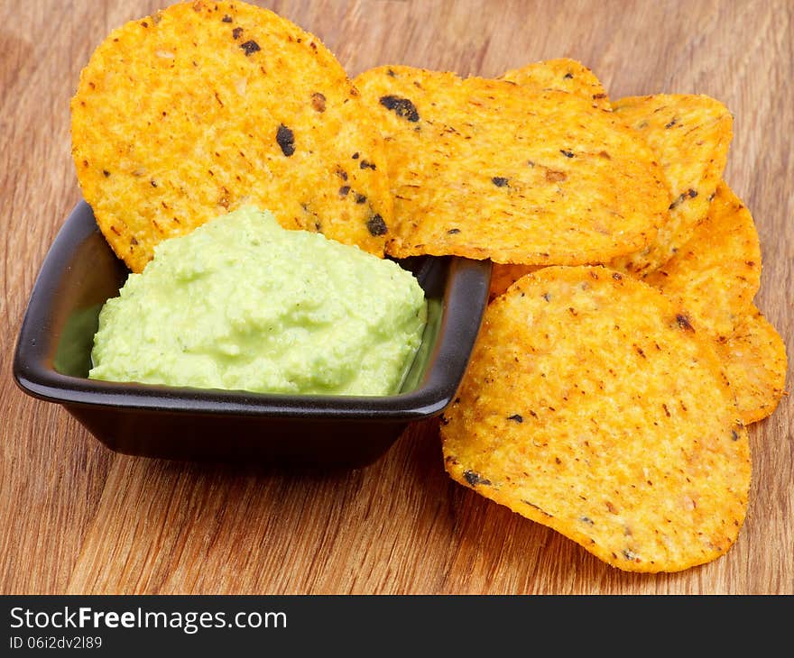 Arrangement of Tortilla Chips and Guacamole Sauce in Black Bowl closeup on Wooden background