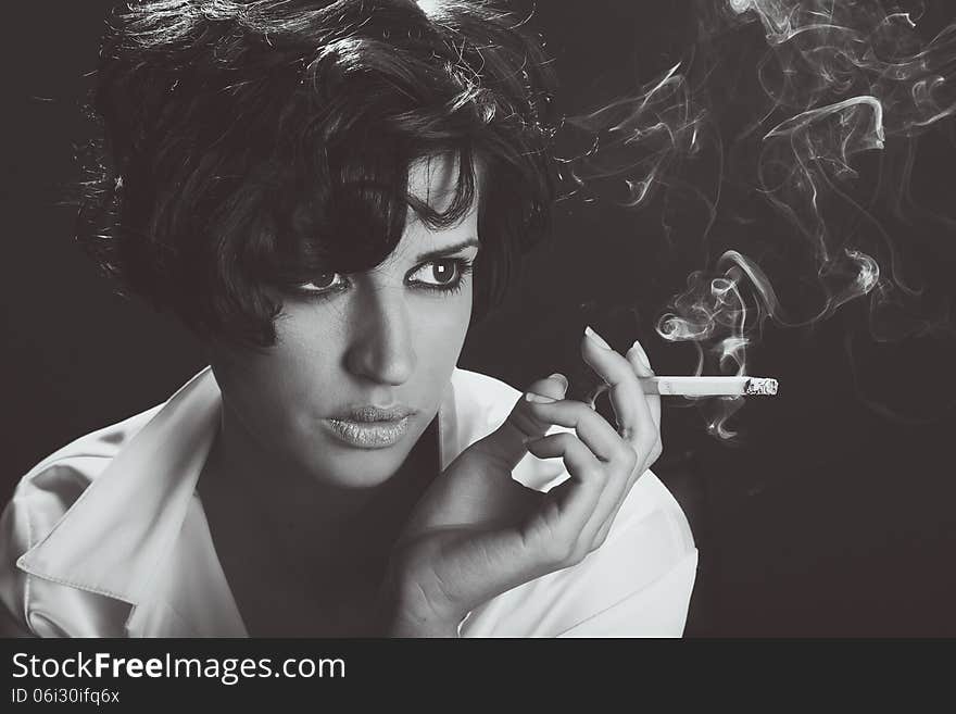 Elegant brunette woman smoking a cigarette on black background