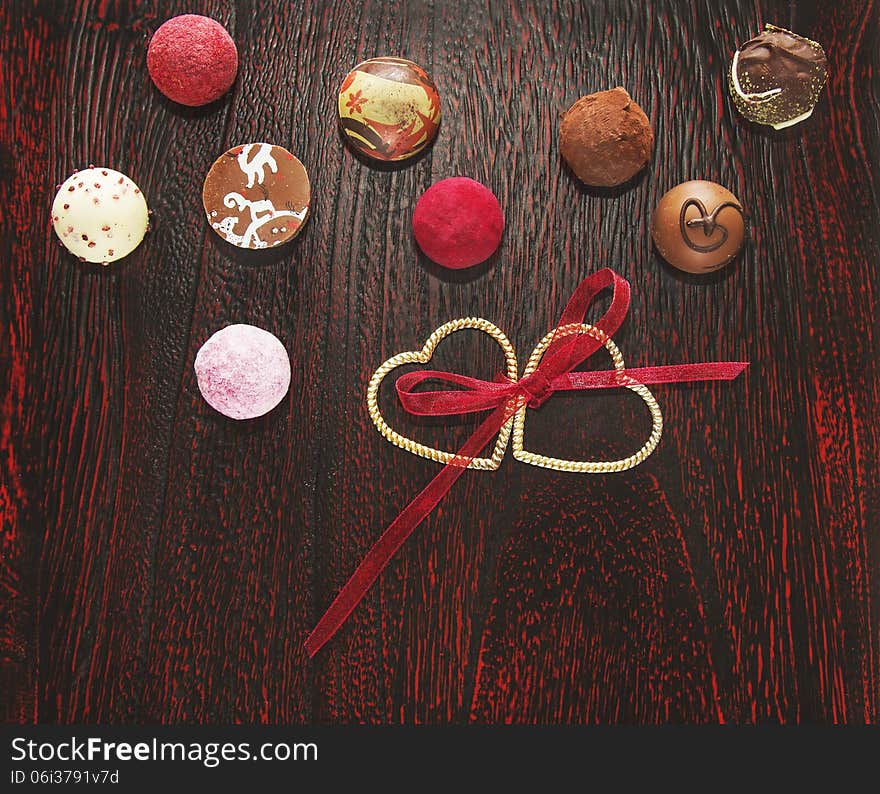 Colorful pralines candies with two hearts and ribbon wooden floor