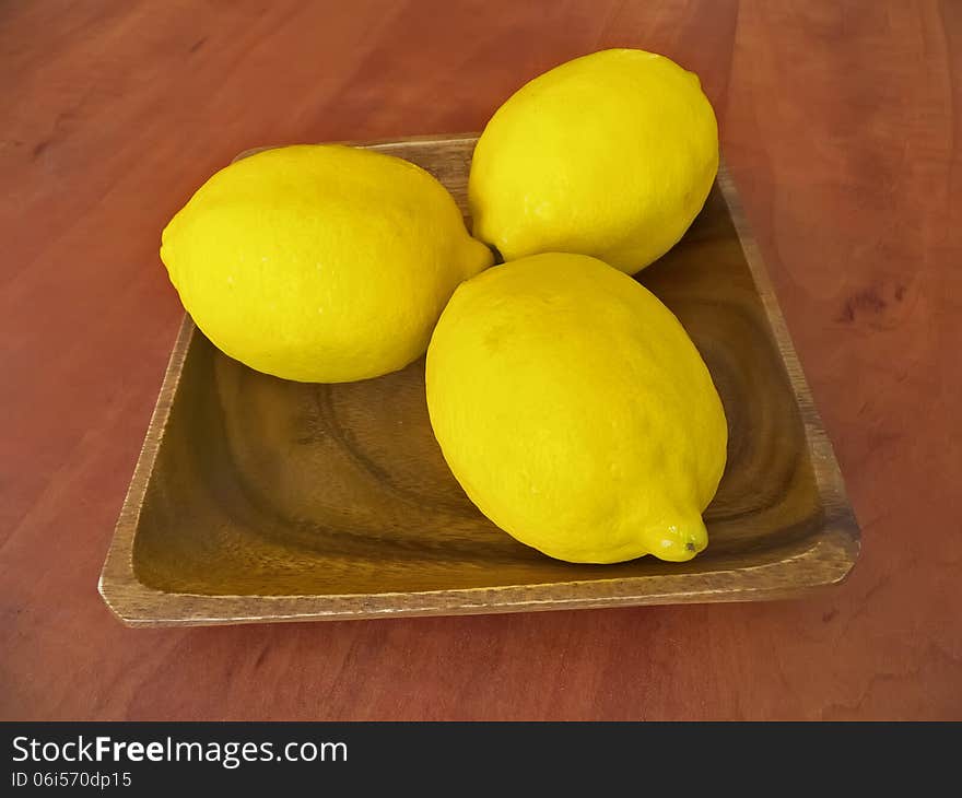 Three fresh lemons on a wooden plate on a table.