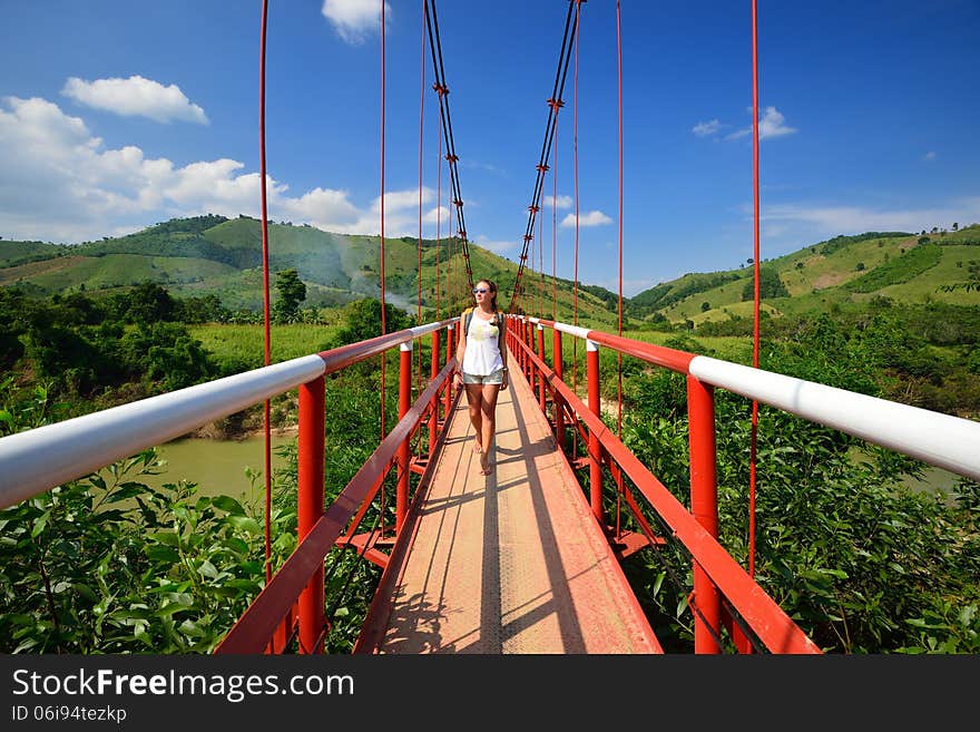 Traveler passes the river on a suspension bridge on the background of green mountains. Vietnam. Traveler passes the river on a suspension bridge on the background of green mountains. Vietnam