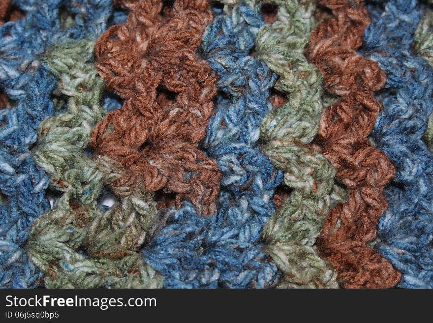 Closeup of crochet fabric with vertical blue, green, and brown stripes. Closeup of crochet fabric with vertical blue, green, and brown stripes.