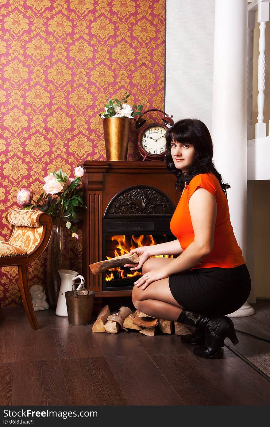 Young beautiful woman in orange blouse sits near the fireplace. Young beautiful woman in orange blouse sits near the fireplace