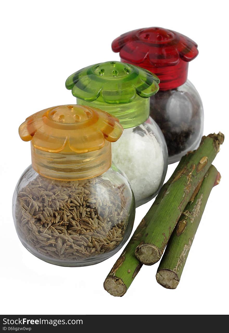 Three glass jars with multi-colored covers with spices and green stalks on a white background. Three glass jars with multi-colored covers with spices and green stalks on a white background