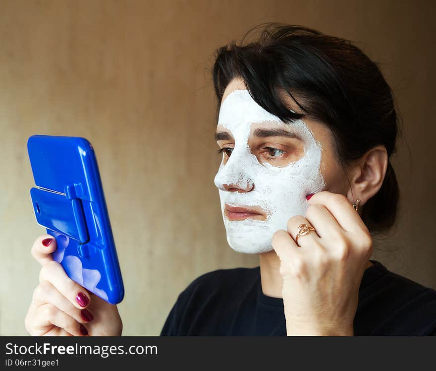 Young beautiful woman gets cosmetic mask in the mirror