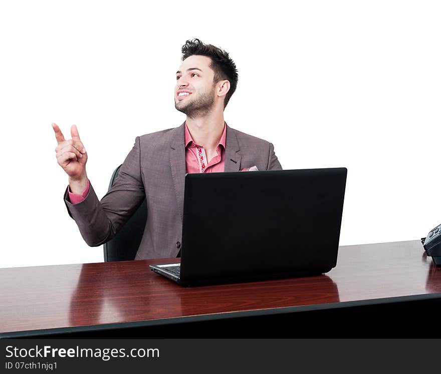 Handsome and smiling business man points with his finger in the air while sitting at his desk with a laptop. Handsome and smiling business man points with his finger in the air while sitting at his desk with a laptop