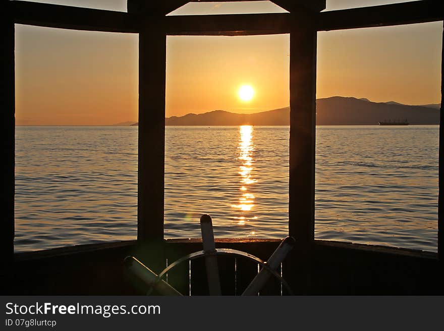 Sunset at Vancouver Bay, Canada, steering wheel and wooden window frame in foreground. Sunset at Vancouver Bay, Canada, steering wheel and wooden window frame in foreground