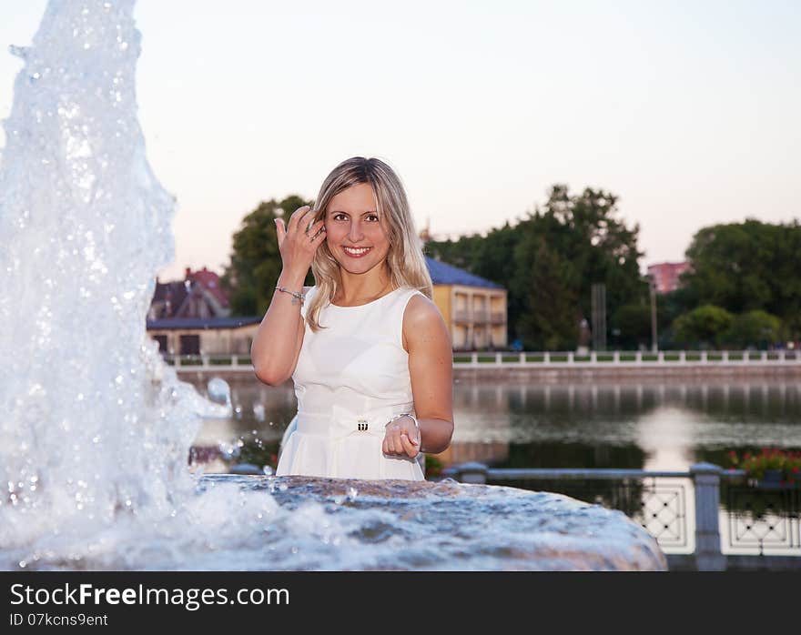 Young beautiful woman in a white dress near the fountain