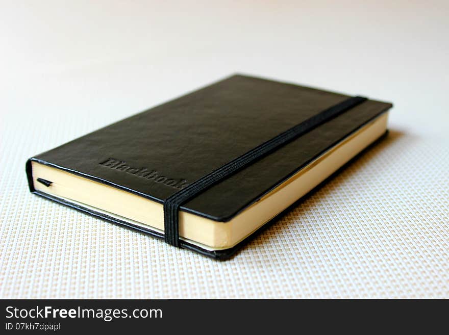 A closed black book lying on a white flooring.