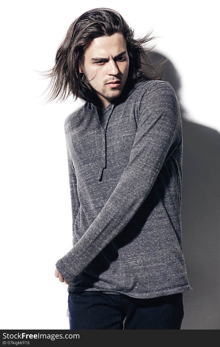 Fashion portrait of young man in gray shirt poses over wall with contrast shadows