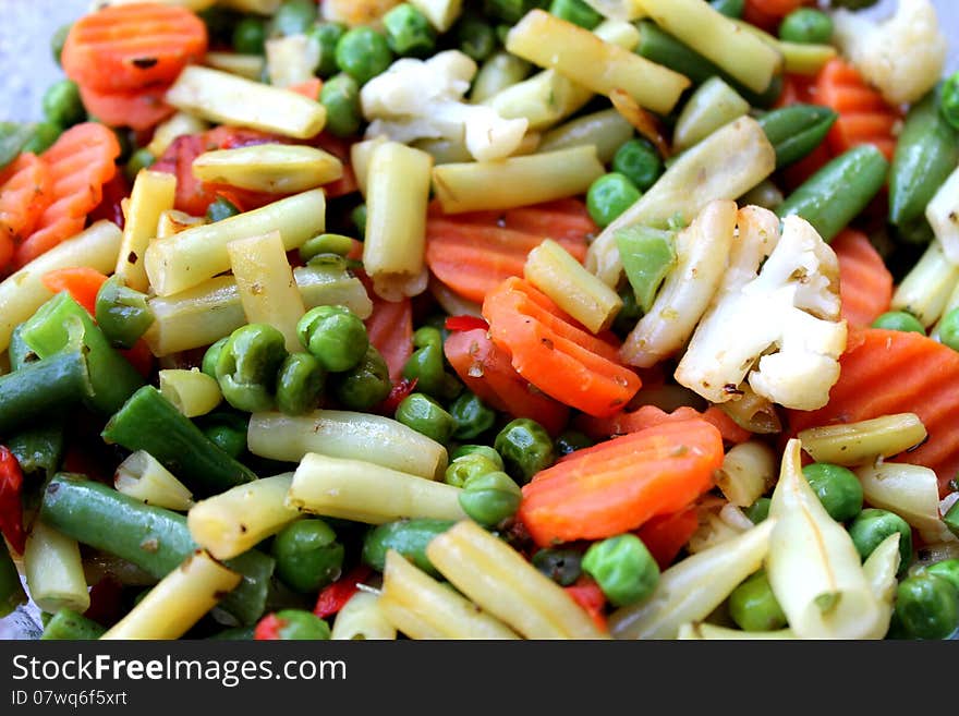 A bowl of colorful assorted vegetables: peas, white beans, green beans, cauliflower, carrots, bell peppers