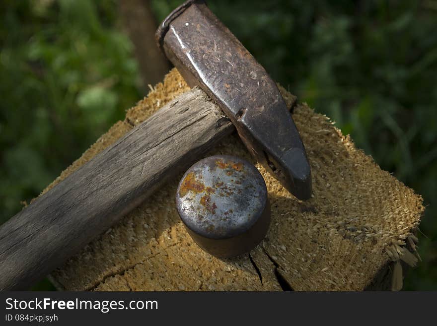 Hammer and iron support for churning scythe placed on wood stand. Hammer and iron support for churning scythe placed on wood stand