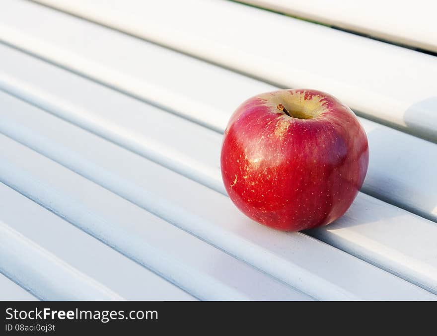 Bright red apple on the bench outside