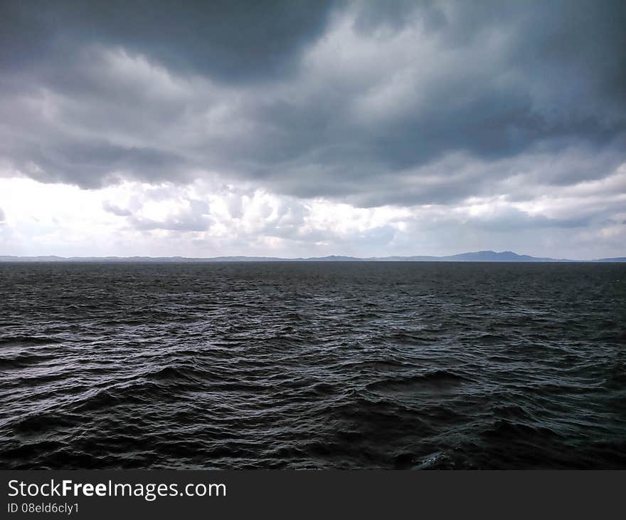 An angry looking black sea with threatening storm clouds overhead and distant hill on the horizon.