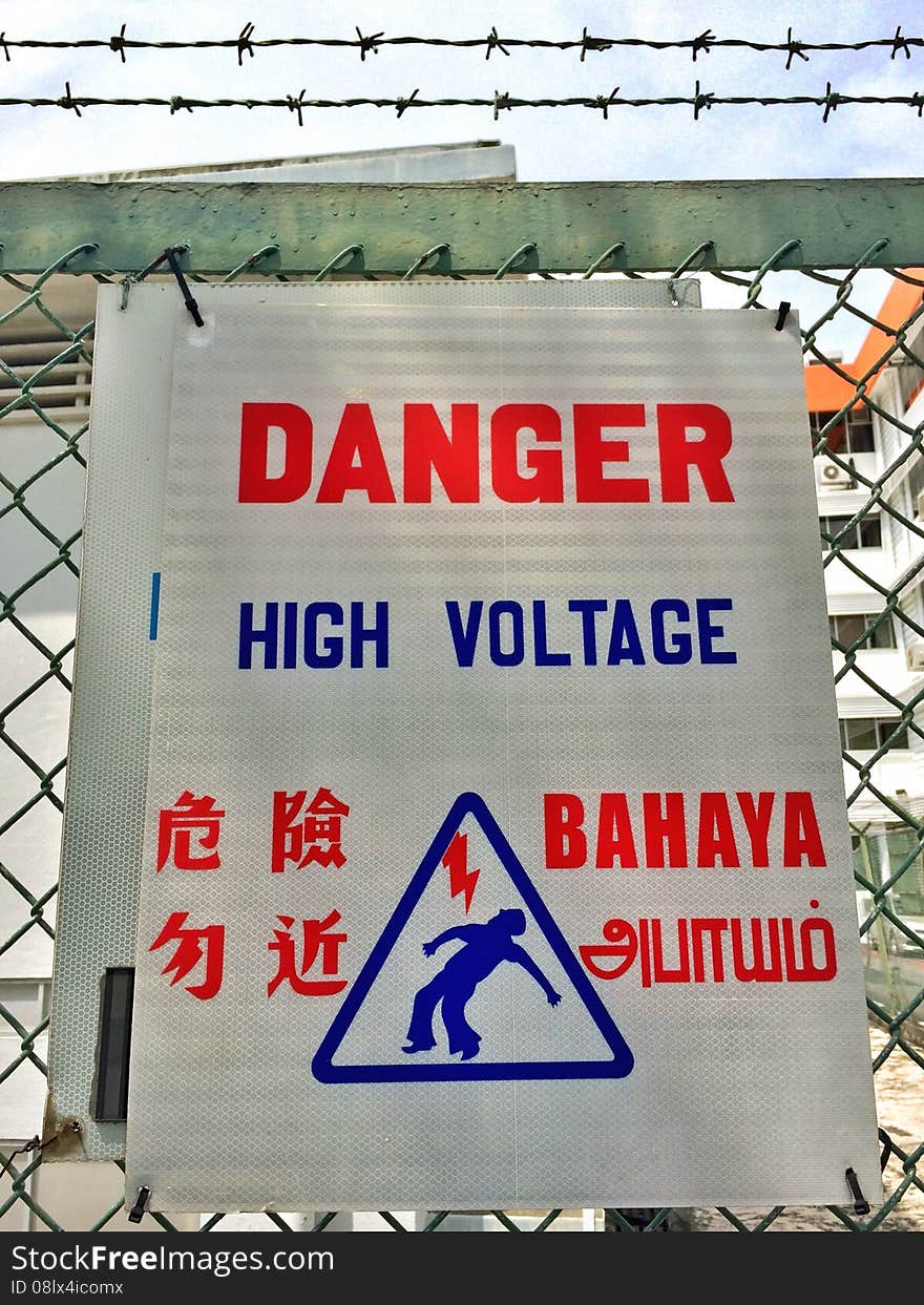 A warning sign outside an electric power supply station fenced with barbed wires. The languages displayed are English, Mandarin, Malay and Tamil. A warning sign outside an electric power supply station fenced with barbed wires. The languages displayed are English, Mandarin, Malay and Tamil.