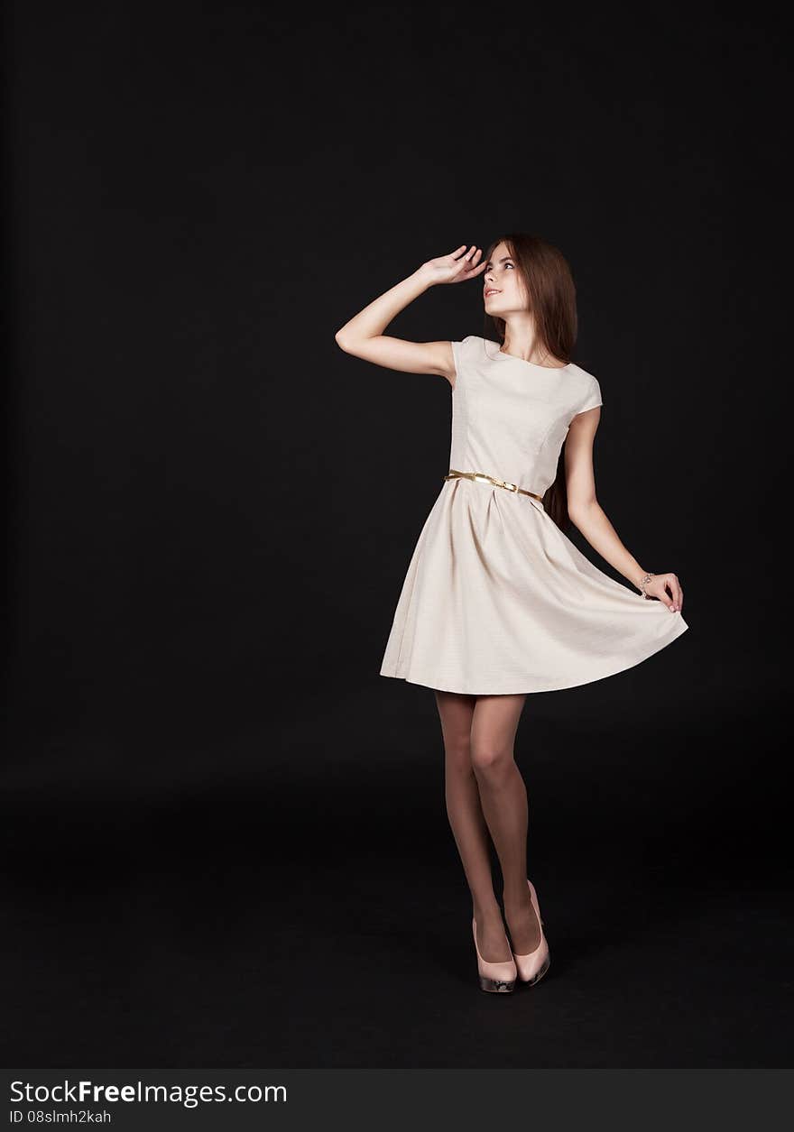 Young beautiful girl in a light dress looking up in studio on black background