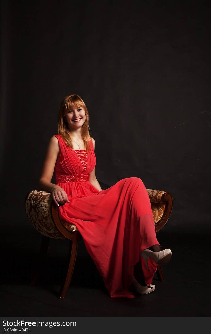 Young beautiful smiling woman in red dress sitting on a chair