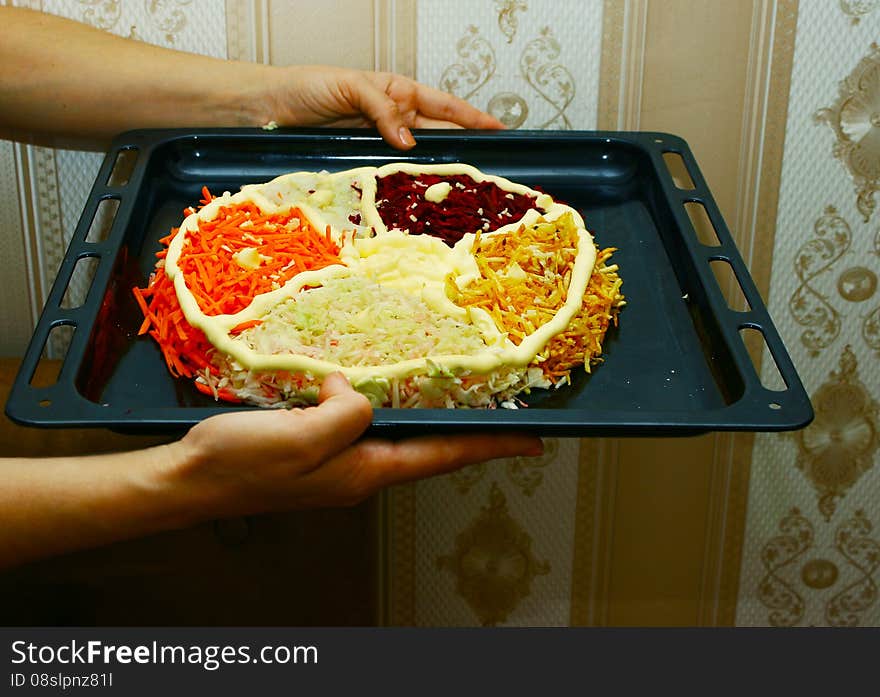 Woman is holding a baking sheet with a salad in the form of cake