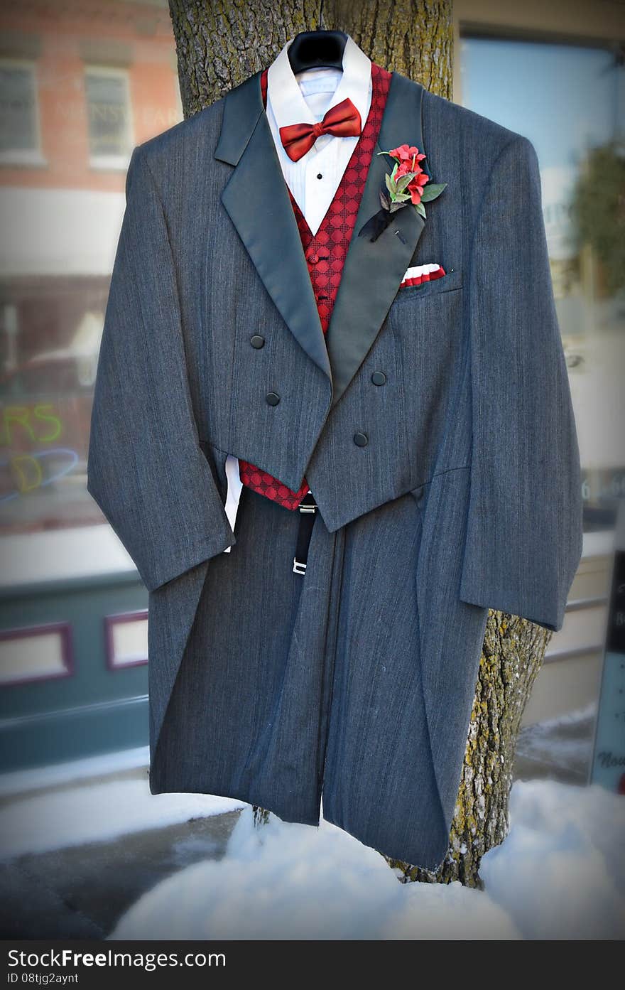 A formal Tuxedo with red vest and red bowtie and floral boutineer, hanging on a tree with snow on the ground in front of a men's formal wear store in Burlington, Wisconsin. Racine County - United States of America. A formal Tuxedo with red vest and red bowtie and floral boutineer, hanging on a tree with snow on the ground in front of a men's formal wear store in Burlington, Wisconsin. Racine County - United States of America.