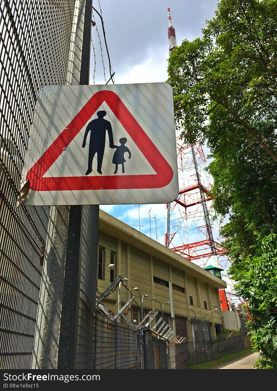 A signboard showing parent holding child's hand to remind pedestrians to look after the younger ones when crossing or walking along the road around Bukit Batok Nature Park. A signboard showing parent holding child's hand to remind pedestrians to look after the younger ones when crossing or walking along the road around Bukit Batok Nature Park