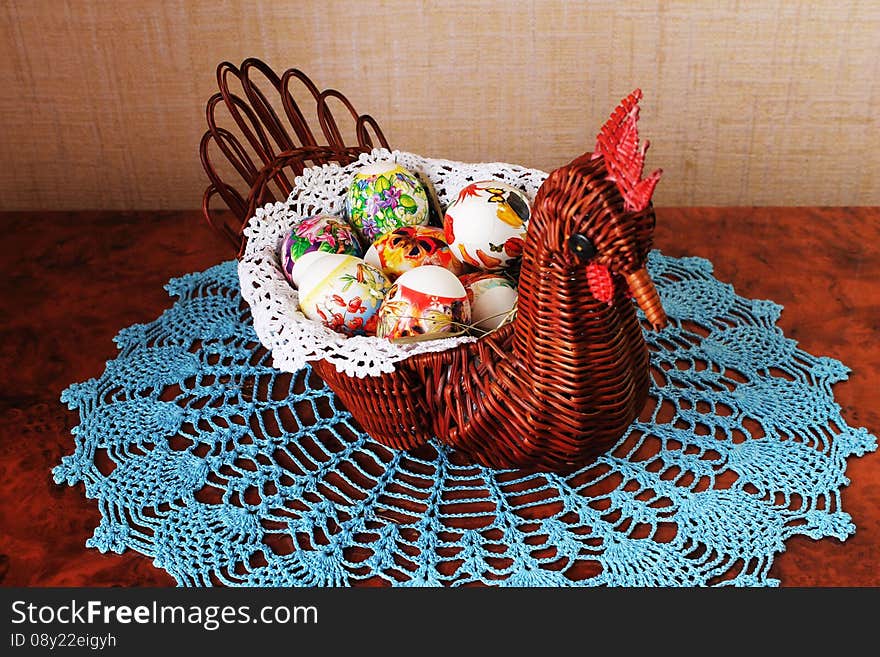 Decorative wicker vase in the form of chicken with Easter eggs inside on lacy napkin. Decorative wicker vase in the form of chicken with Easter eggs inside on lacy napkin