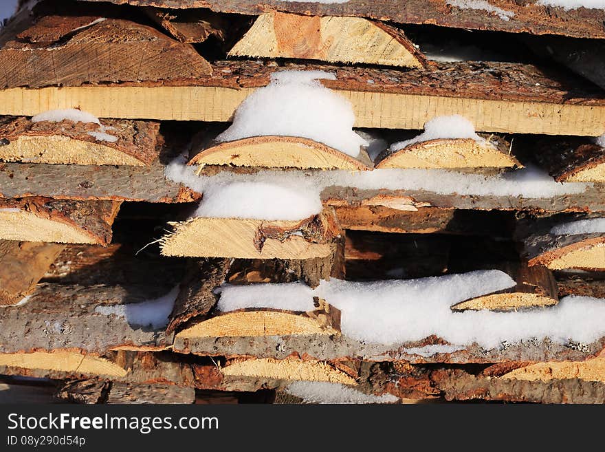 Background of stacked firewood in woodpile powdered white snow