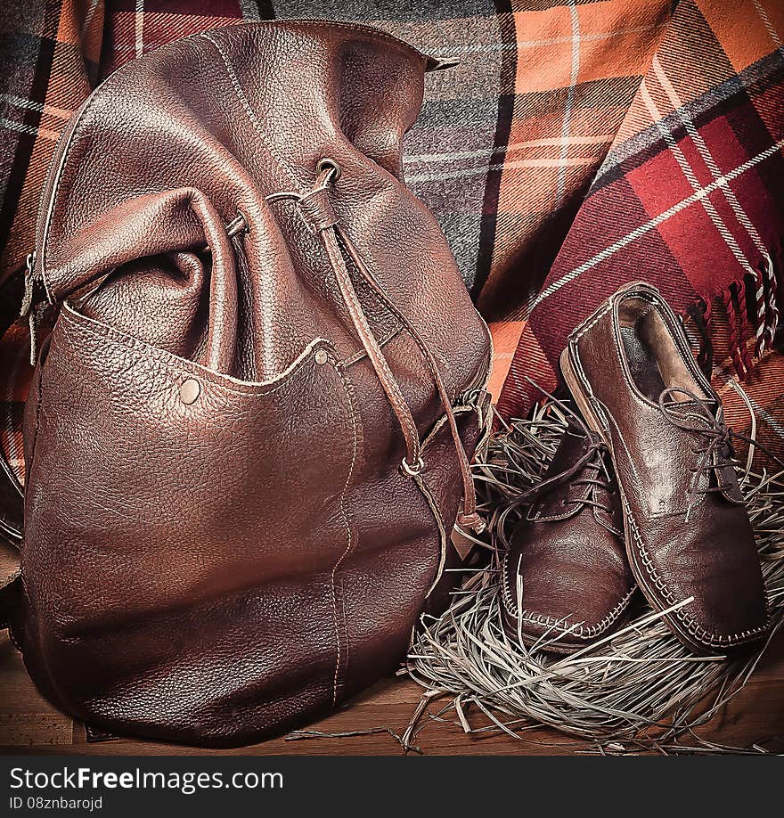 Leather backpack and shoes on the background of wool tartan on the wooden floor. Leather backpack and shoes on the background of wool tartan on the wooden floor