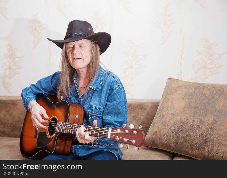 Middle-aged man in a hat plays guitar and sings at home