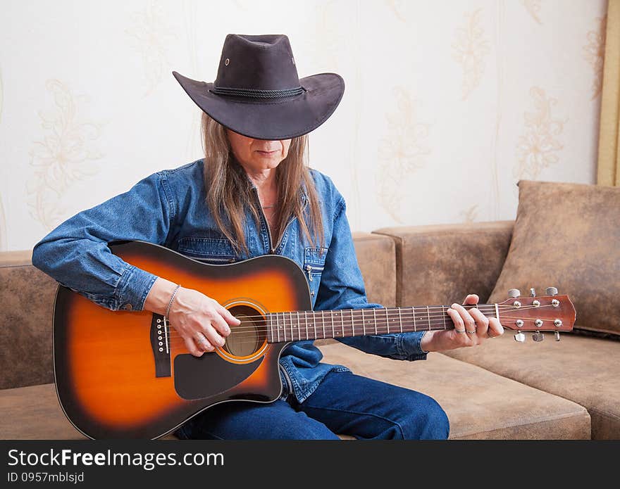 Elderly man in a hat playing guitar at home