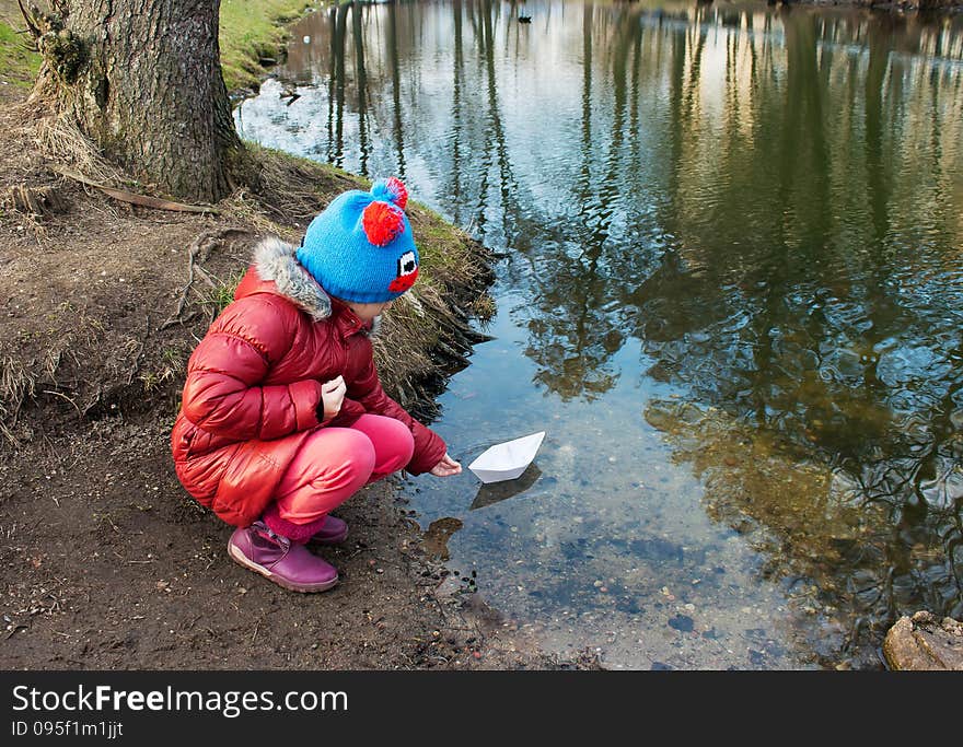 Little girl let a paper boat on the river outside