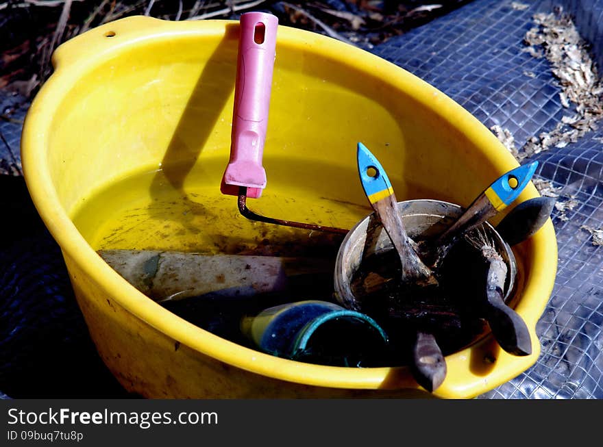 Yellow plastic basin of water, brushes and rusty paint roller. Close up in sunny day.