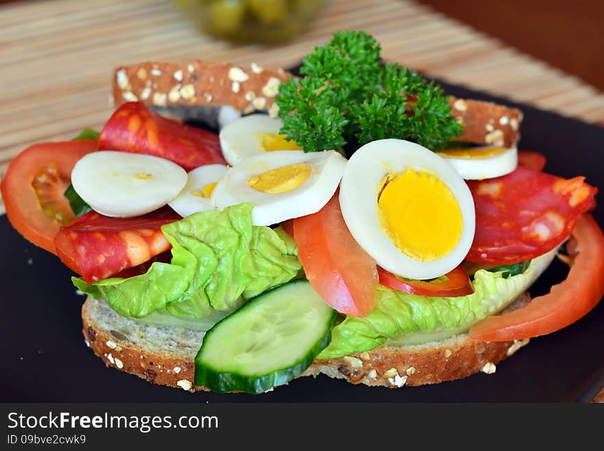 Fresh and tasty sandwich with salami and vegetables on a brown plate on a table. Fresh and tasty sandwich with salami and vegetables on a brown plate on a table