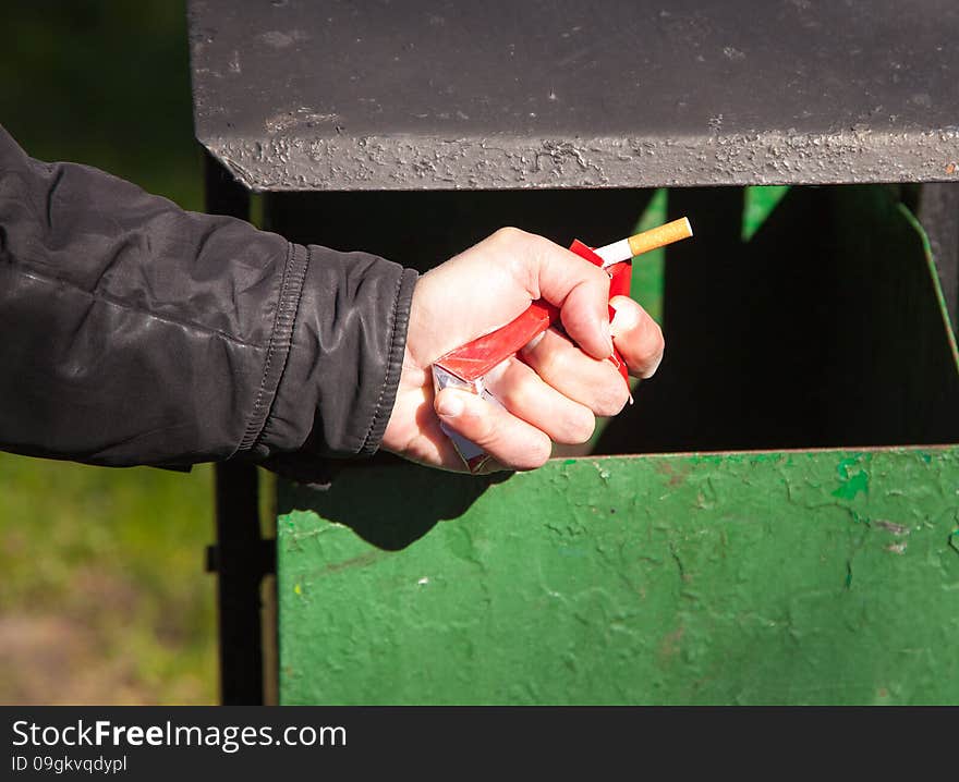 Man&#x27;s hand breaks a pack of cigarettes about a waste bin closeup outside