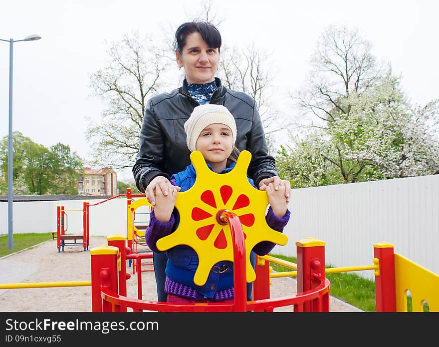 Mom plays with her daughter at the playground on a toy ship