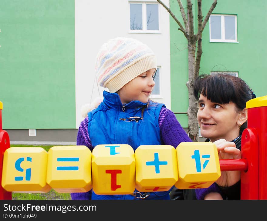 Mom teaches daughter to be considered at the playground with wooden cubes on spring day outside. Mom teaches daughter to be considered at the playground with wooden cubes on spring day outside