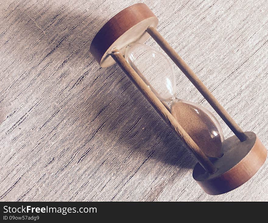 A wooden hourglass placed on a canvas textile. A wooden hourglass placed on a canvas textile.