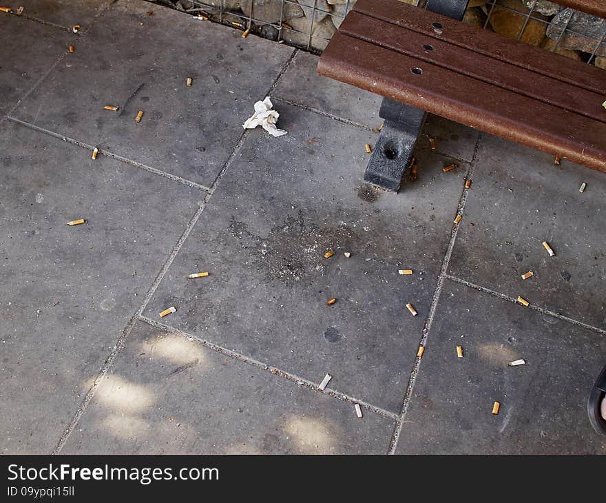 Dirt, litter and cigarette butts next to a city street public bench