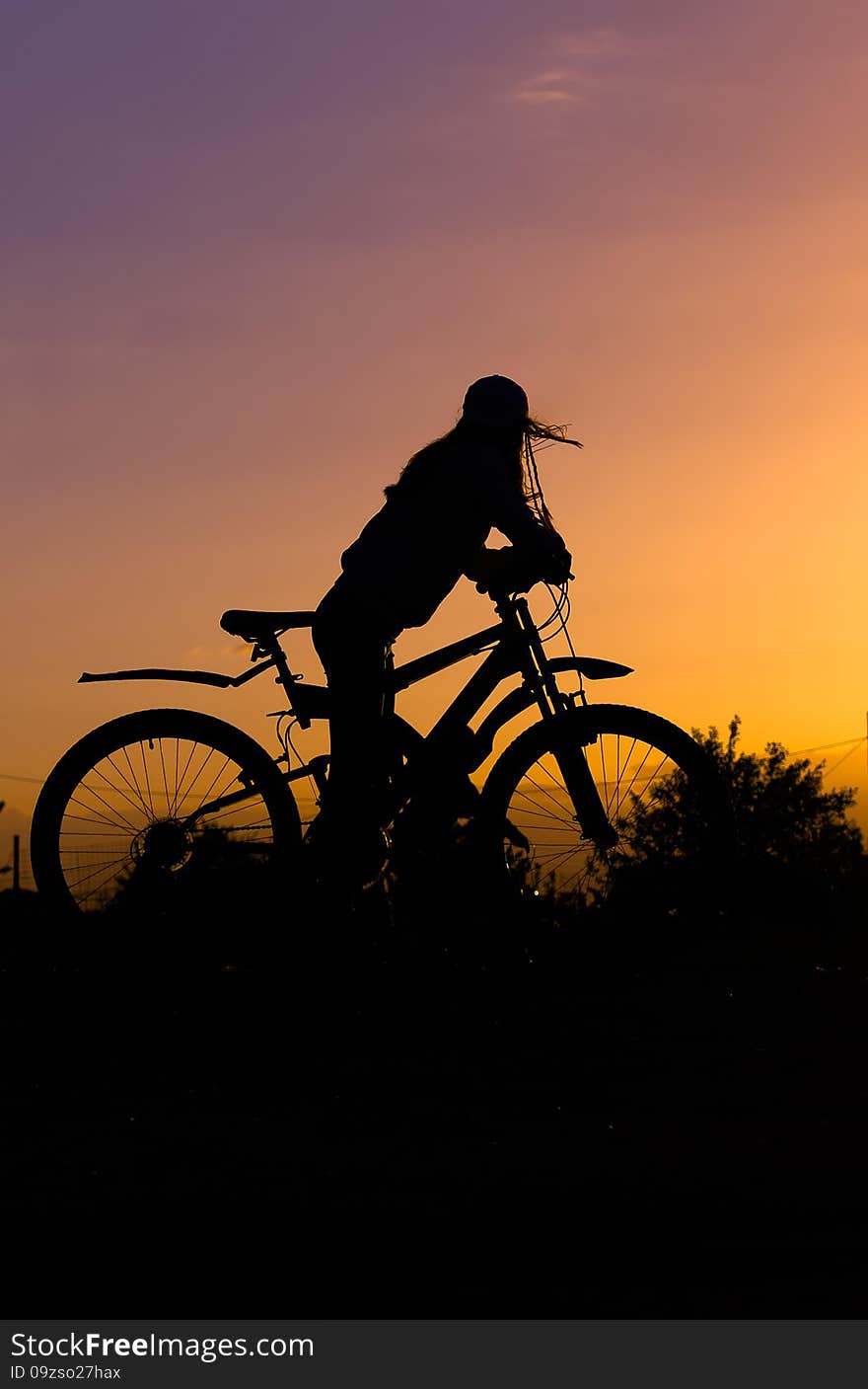 Silhouette of a gerl with a bicycle against the sky at sunset