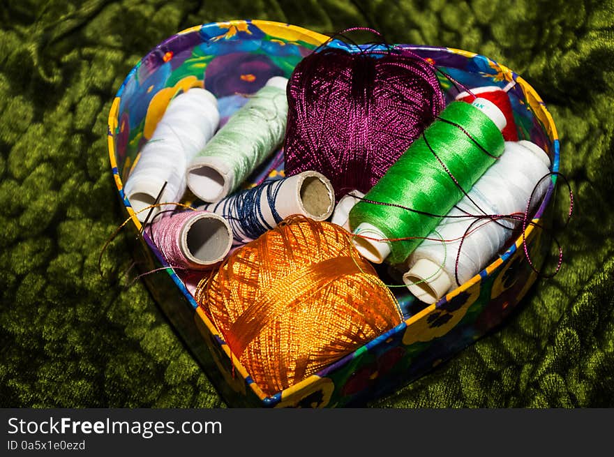 Colorful box with floral cover full of colorful spools of thread. Colorful box with floral cover full of colorful spools of thread