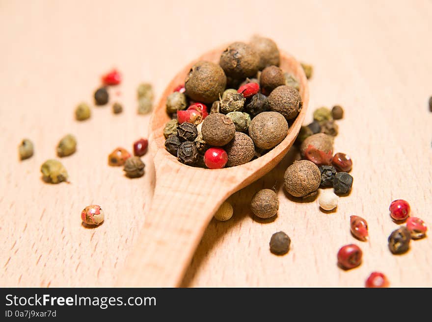 Spoon filled with a mixture of grains of pepper are on a wooden